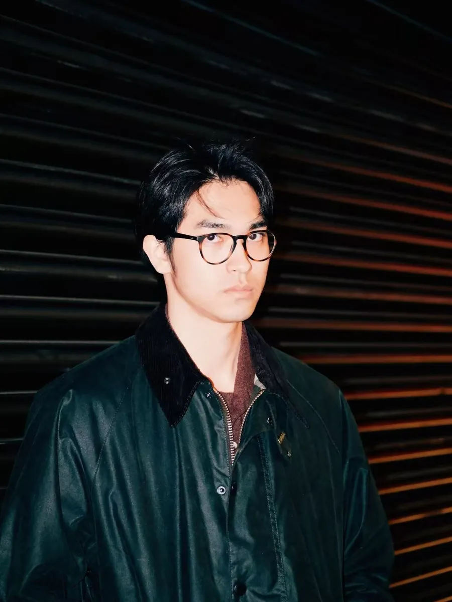 Rui Yang in a dark jacket and glasses in front of a ribbed wall