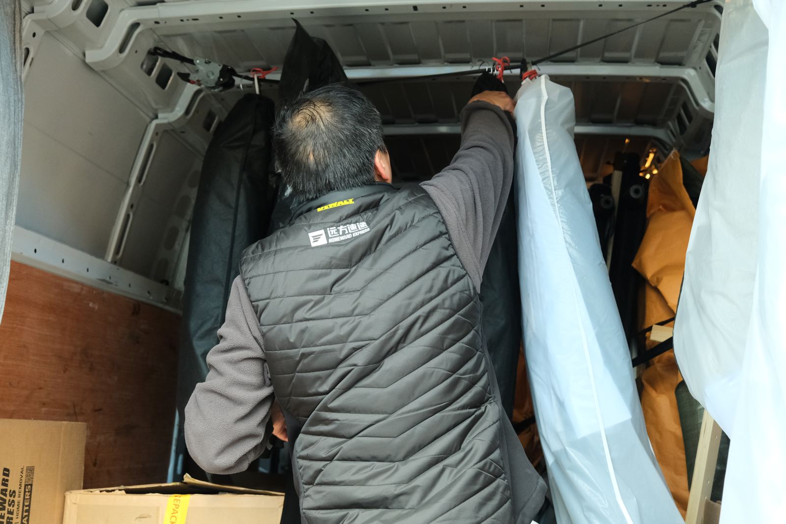 A driver hanging garment bags on a strap across the roof inside the van.