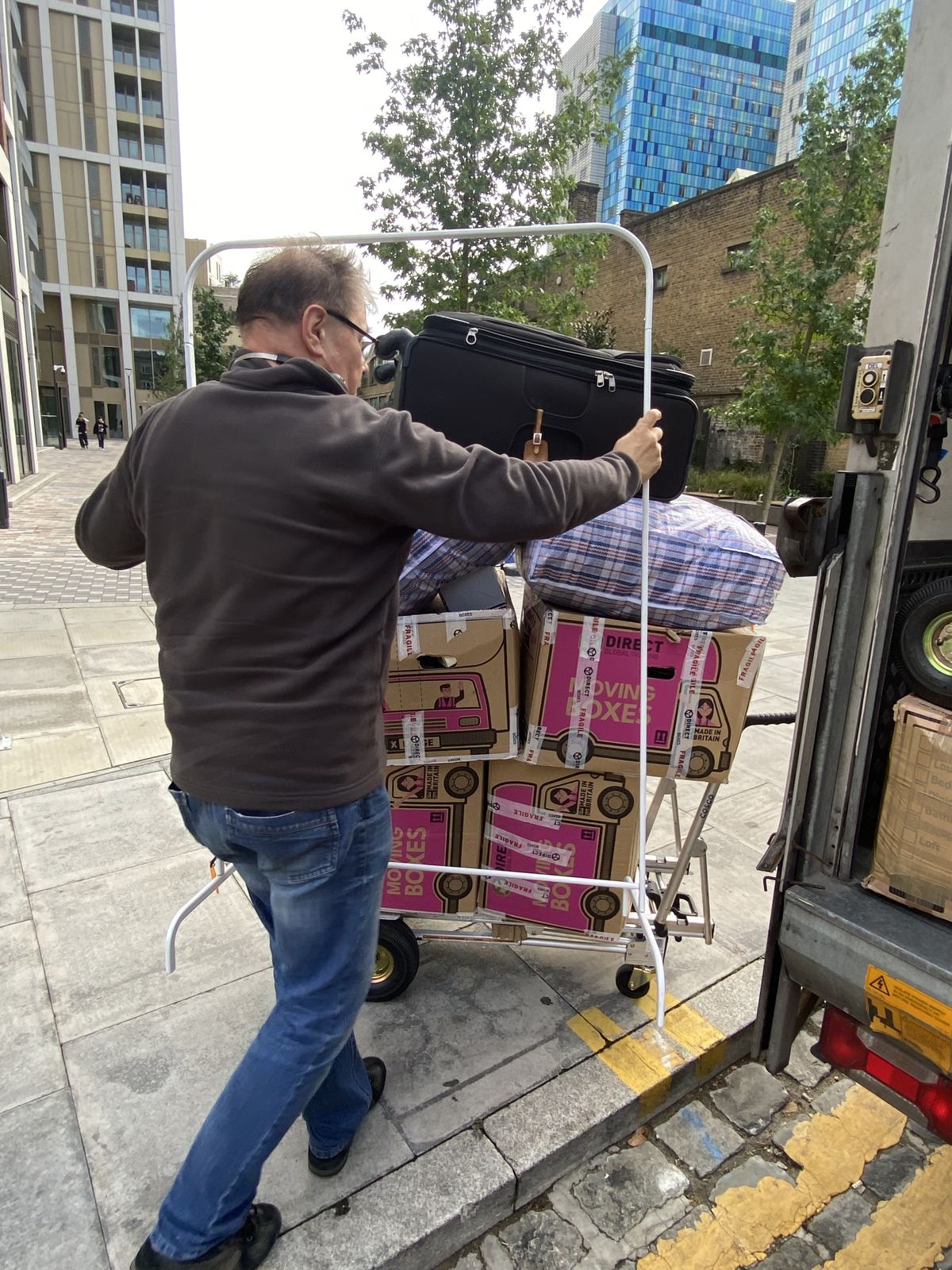 A driver wheeling moving boxes, bags and a clothes rail to the back of a Luton van.