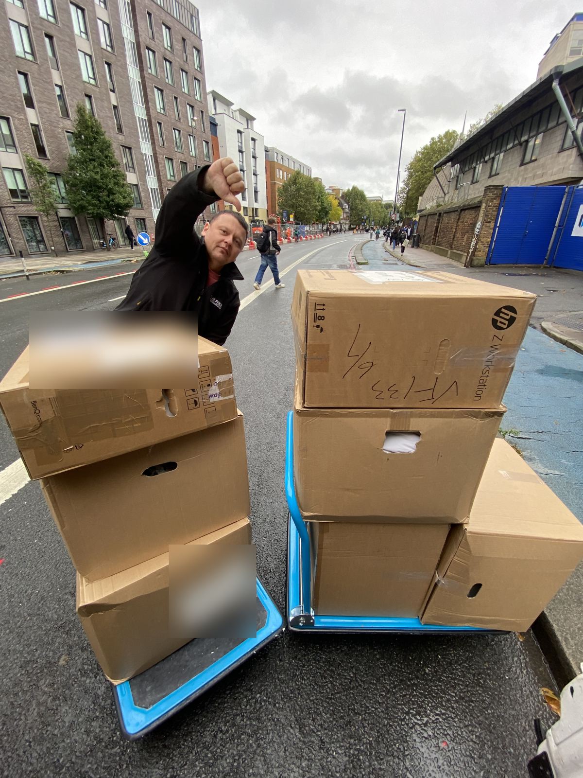 A driver giving a thumbs down behind two trolleys of boxes on a main road with a bus lane.