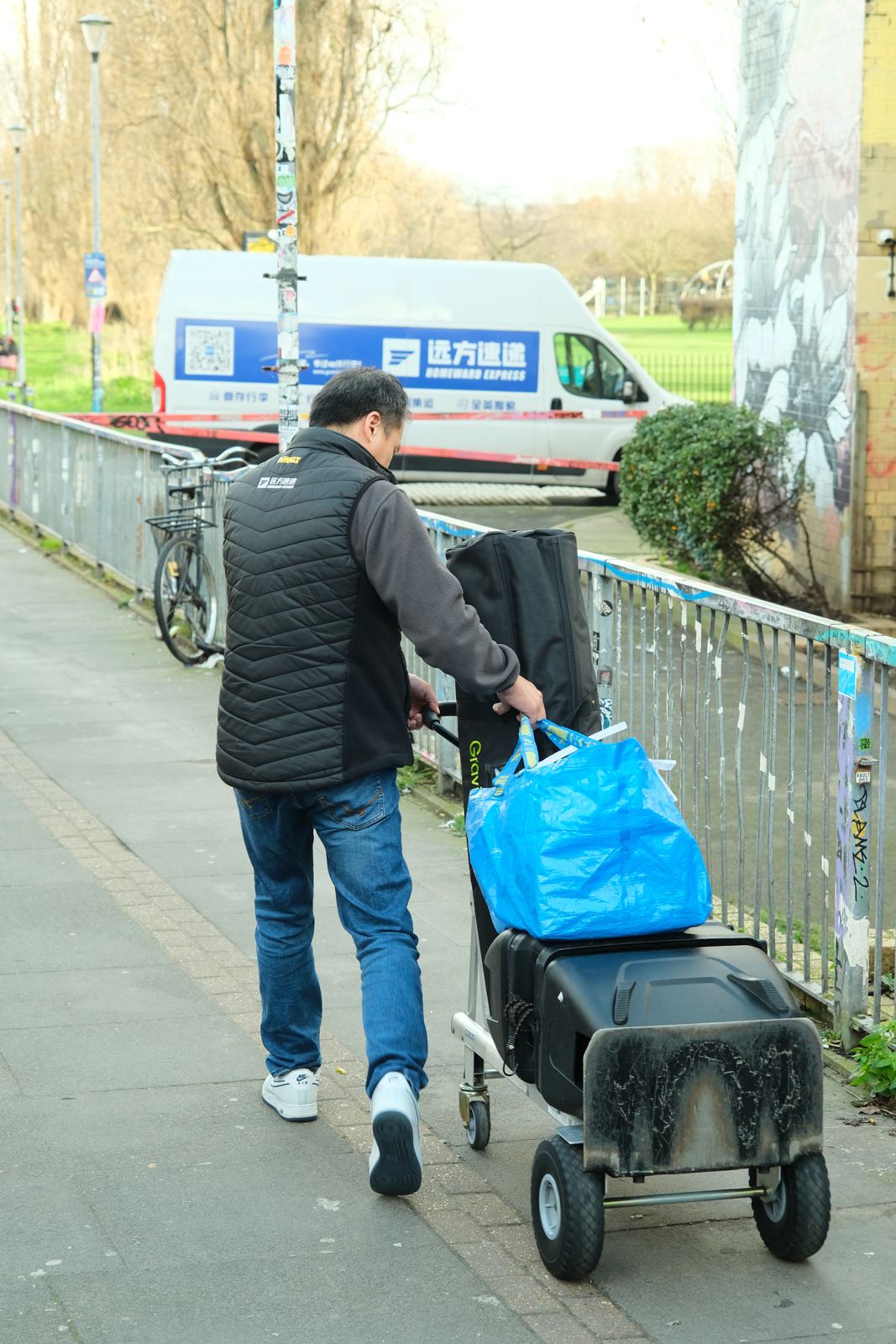 A driver pulling a hand truck of luggage along a path, the company van parked behind