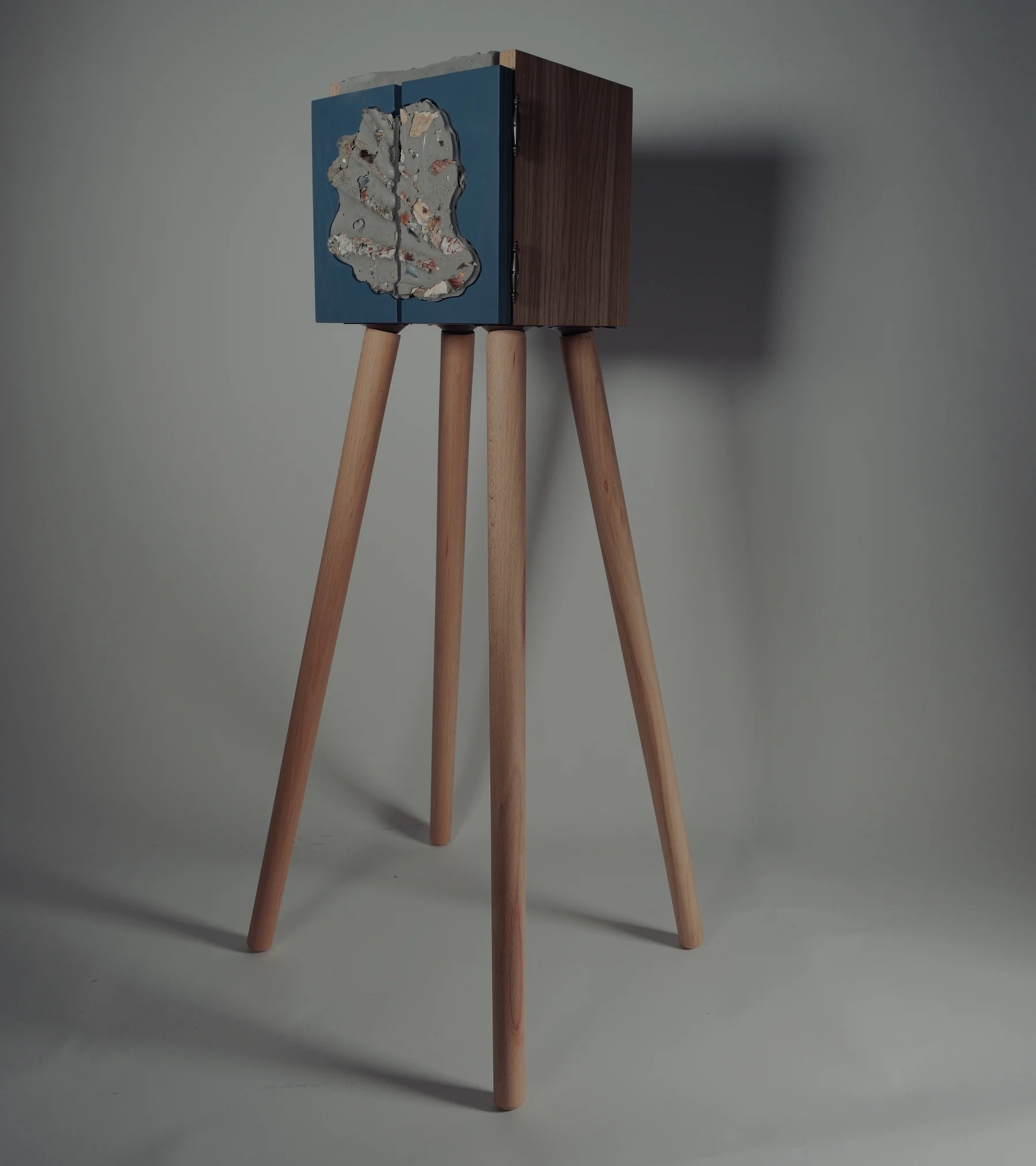 The finished Shell cabinet on four tall wooden legs, with blue doors set with a shell-concrete tile