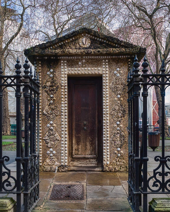 A shell-covered hut in Grosvenor Gardens, London, seen through iron gates