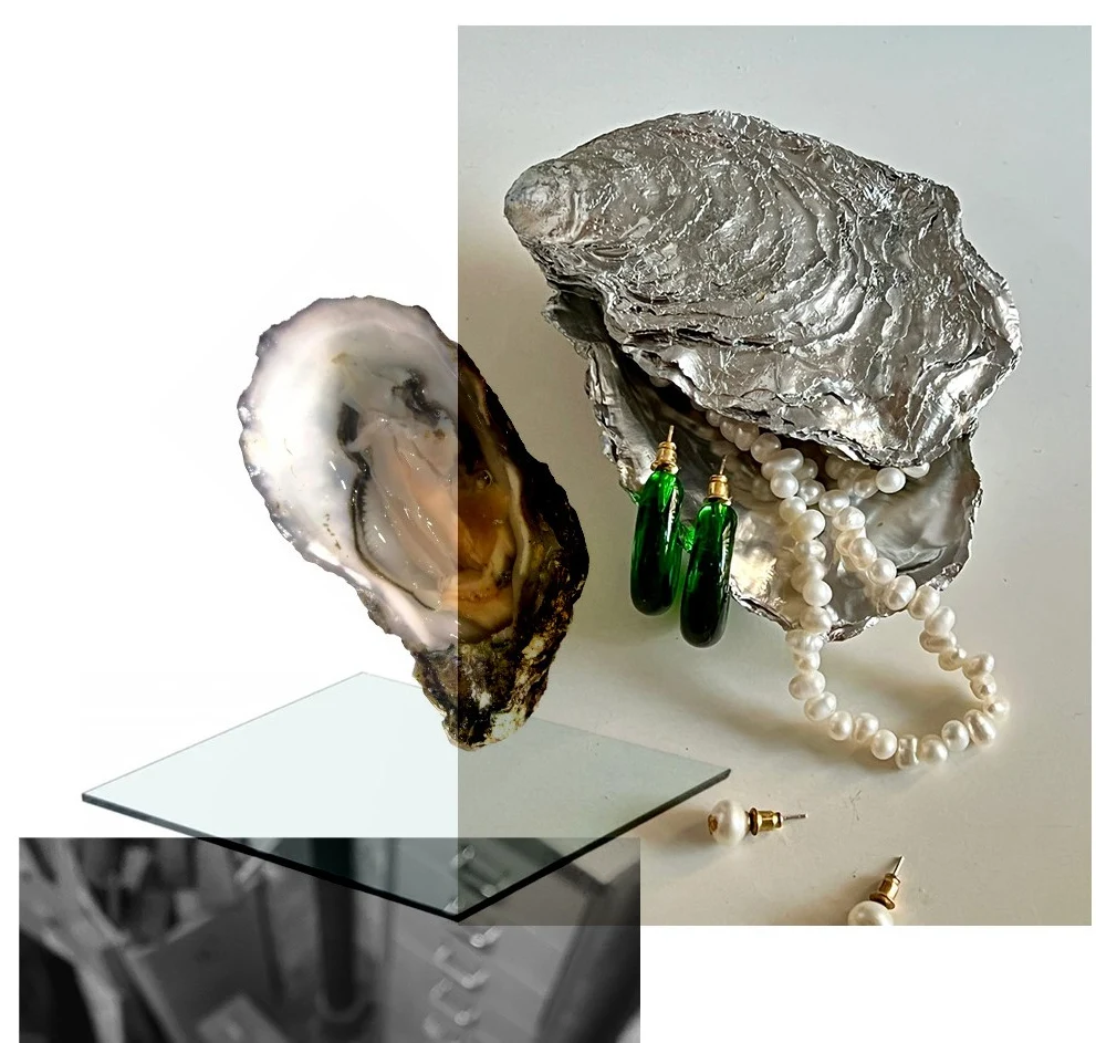 Silver-sprayed oyster shells holding pearls and earrings, on a glass shelf
